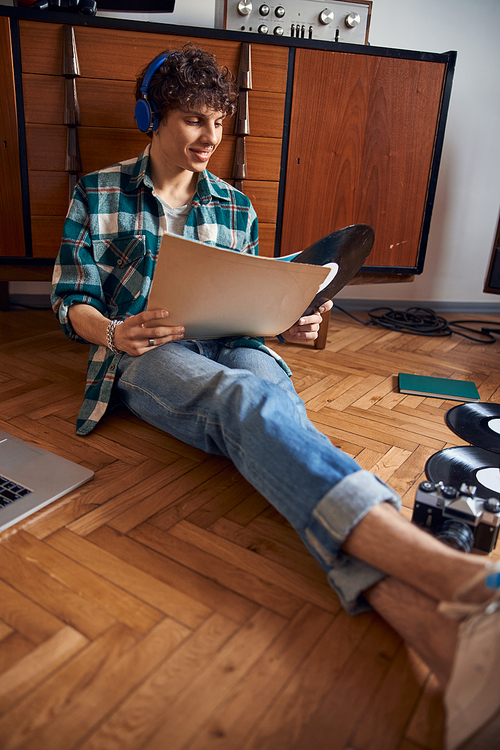 Smiling young man sitting on the floor and holding vinyl record stock photo