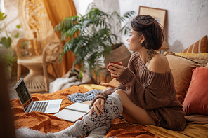 Side view of lady sitting in bedroom and holding cup stock photo
