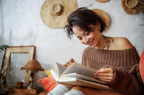 Smiling lady holding book on legs in bedroom stock photo