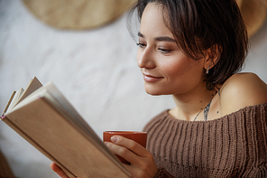 Cropped photo of nice lady looking into book and holding cup