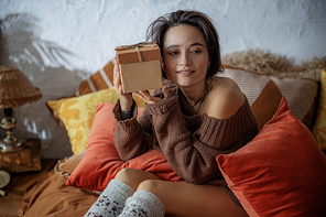 Happy woman holding present near her face in bedroom stock photo