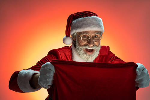 Smiling senior Santa Claus wearing in costume and looking inside sack with presents