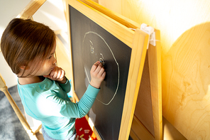 Adorable child using colorful chalks to draw on blackboard at home stock photo
