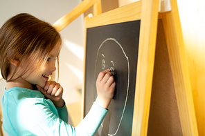 Cute joyful kid using colorful chalks to draw on blackboard stock photo