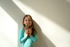 Cute child with colored drawing pencils standing against white wall stock photo. Website banner