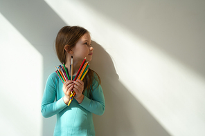 Adorable kid with colorful drawing pencils standing against white wall stock photo. Website banner