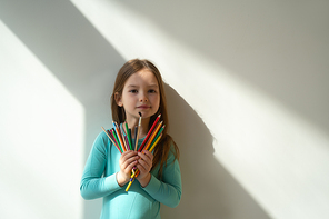 Cute kid with colorful drawing pencils standing against white wall stock photo. Website banner