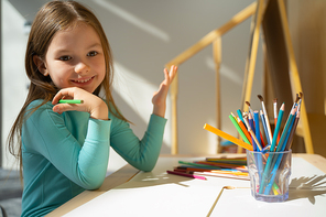 Cute kid sitting at the table with colorful pencils and smiling stock photo