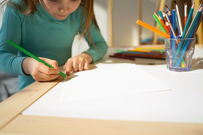 Cute child sitting at wooden desk and drawing with green pencil stock photo