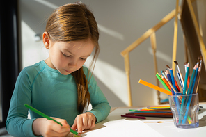 Adorable child sitting at the table and drawing with green pencil stock photo