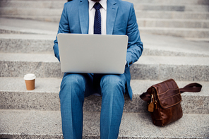 Cropped photo of a stylish Caucasian businessman with a notebook on his knees working outside