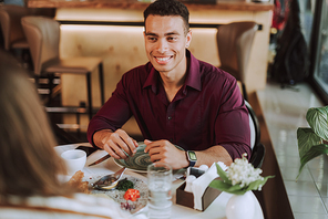 Good-looking gentleman in elegant shirt sitting at the table and smiling while looking at his friend