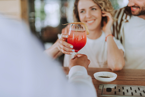 Close up of bartender serving cocktail to smiling lady while she sitting at the counter with her boyfriend. Focus on hands with beverage