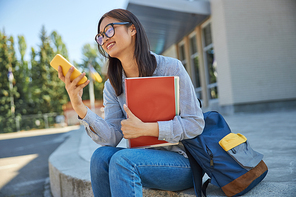 Smiling female student with smartphone near college stock photo