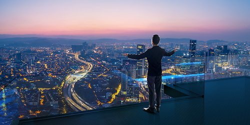 Businessman standing on open roof top balcony watching city night view . Business ambition and vision concept .