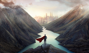 Businessman in a suit and cape hero on top of the hill watching wonderful scenery in mountains with lake during dramatic sunrise .Business ambition and success concept.