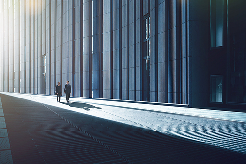 Two young businessmen walking in the streets of facade with metal and stripes design construction in modern building .