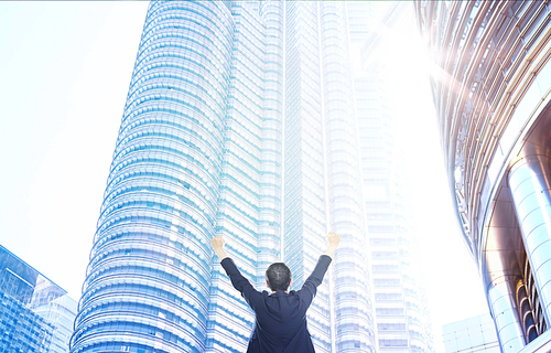 Businessman raises hands up excited with skyscraper background