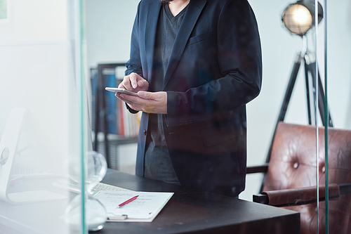 Unrecognizable young hipster businessman using his smartphone standing in cozy office