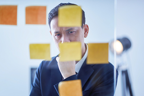 Asian pensive businessman  looking at glass wall with sticker notes , brainstorming concept .
