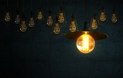 Hanging retro light bulbs decor on dark blue cement background with one isolated glowing .