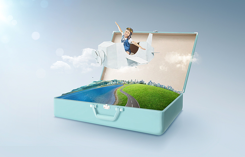 Little asian girl enjoy with fantasy cardboard plane fly and floating in an open retro vintage suitcase isolated on light blue background . Travel and vacation concept.