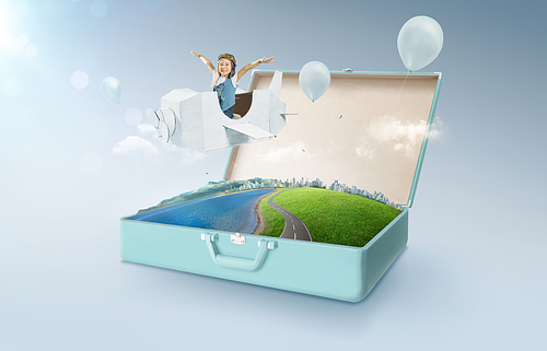 Little asian girl enjoy with fantasy cardboard plane fly and floating in an open retro vintage suitcase isolated on light blue background . Travel and vacation concept.