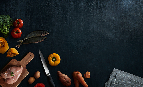 Various healthy raw food and ingredients ready for cooking on black wooden background . Delicious and tasty food cooking concept . Top view .