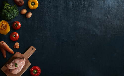 Various healthy raw food and ingredients ready for cooking on black wooden background . Delicious and tasty food cooking concept . Top view .