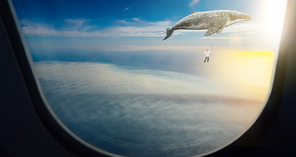 Whale floats in the air above the clouds carrying a young guy ,seen through window of an aircraft , dreams and travel concept .