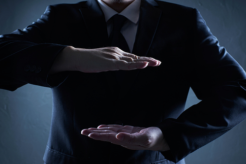 Businessman in suit with two hands in position to protect something (focus on hand, blur out the suit).