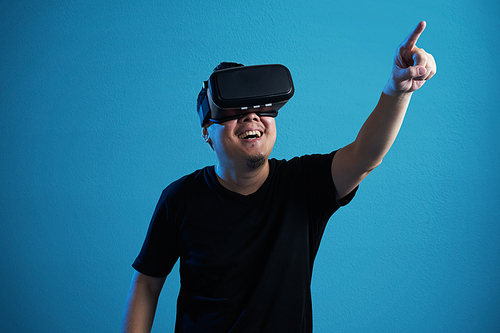 Asian man wearing virtual reality goggle and pointing up .