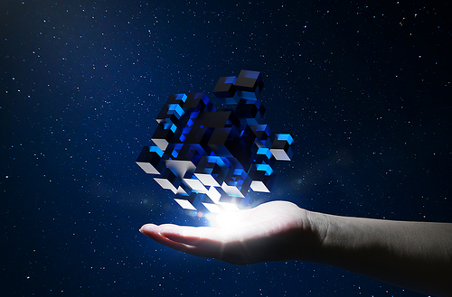 Unknown hand holding floating blue shiny cube on dark background .