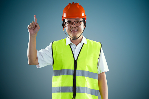 Young asian construction workers in safety helmet pointing up the finger ,isolated on blue background .