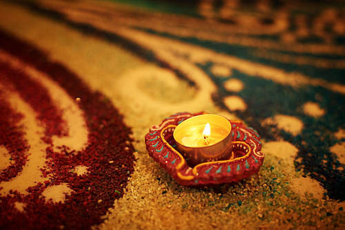 Traditional diya lamp lit on colorful rangoli