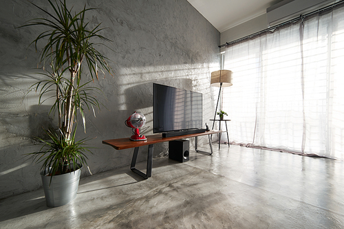 Modern living-room interior with TV in a loft style with wooden TV deck and concrete walls and floor . There are vintage fan ,lamps and green plant to decorate .