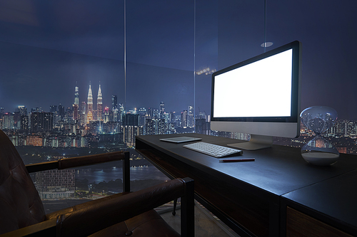 Computer on desktop with Kuala Lumpur city skyline view in dusk.