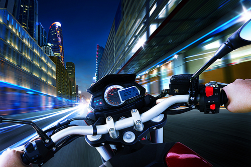 Biker driving a motorcycle rides along the city street , night scene . First person angle view .