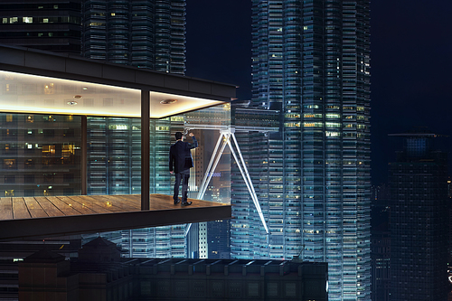 Businessman in an modern sky office by night with beautiful city skyline view .