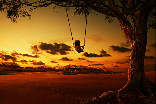 silhouette of happy little girl on a swing with sunset background
