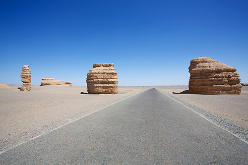 Long empty asphalt road in desert with strange shape of the stone and clear blue sky .