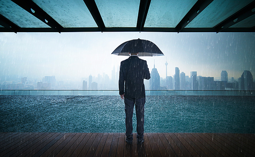 Businessman hold umbrella stand on rooftop ,raining day with city skyline view , risk and crisis concept .