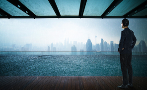 Businessman looking and thinking front of a Swimming pool on roof top with beautiful city skyline view,rainingday .