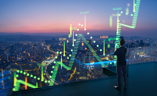 Businessman standing on open roof top balcony watching city night view with stock exchange market graph analysis background effect .  Concept of stock market  .