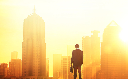 Young smart businessman looking at large city center. Concept of success and appreciation. Standing in front of the spectacular skyline with crowded corporate skyscrapers.
