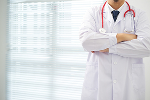 Unknow doctor posing with arms crossed in the office, he is wearing a stethoscope .