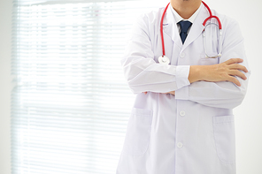 Unknow doctor posing with arms crossed in the office, he is wearing a stethoscope .