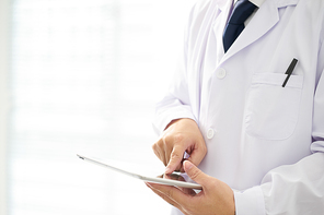 Unknown doctor posing usind digital table with bright background, he is wearing a stethoscope .