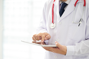 Unknown doctor posing usind digital table with bright background, he is wearing a stethoscope .