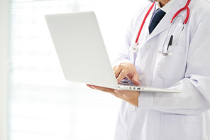 Unknown doctor posing using laptop with bright background, he is wearing a stethoscope .